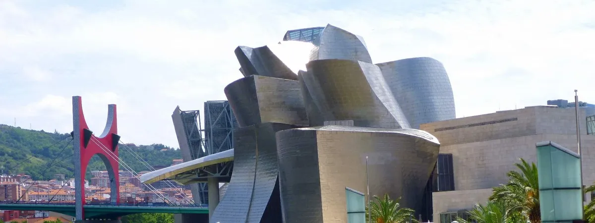 The titanium curves of the Guggenheim Museum Bilbao with the red arches of the La Salve bridge behind