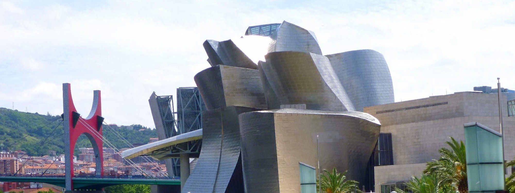 The titanium curves of the Guggenheim Museum Bilbao with the red arches of the La Salve bridge behind