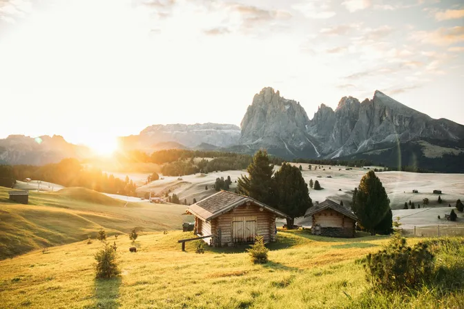 Wooden hay barns on the rolling meadows of Alpe di Siusi at sunrise, with the Sassolungo group behind