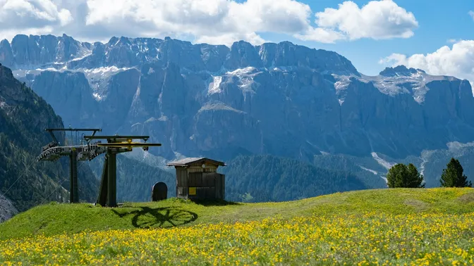 A flower meadow and chairlift in Alta Badia, with the sheer walls of the Sella massif rising behind