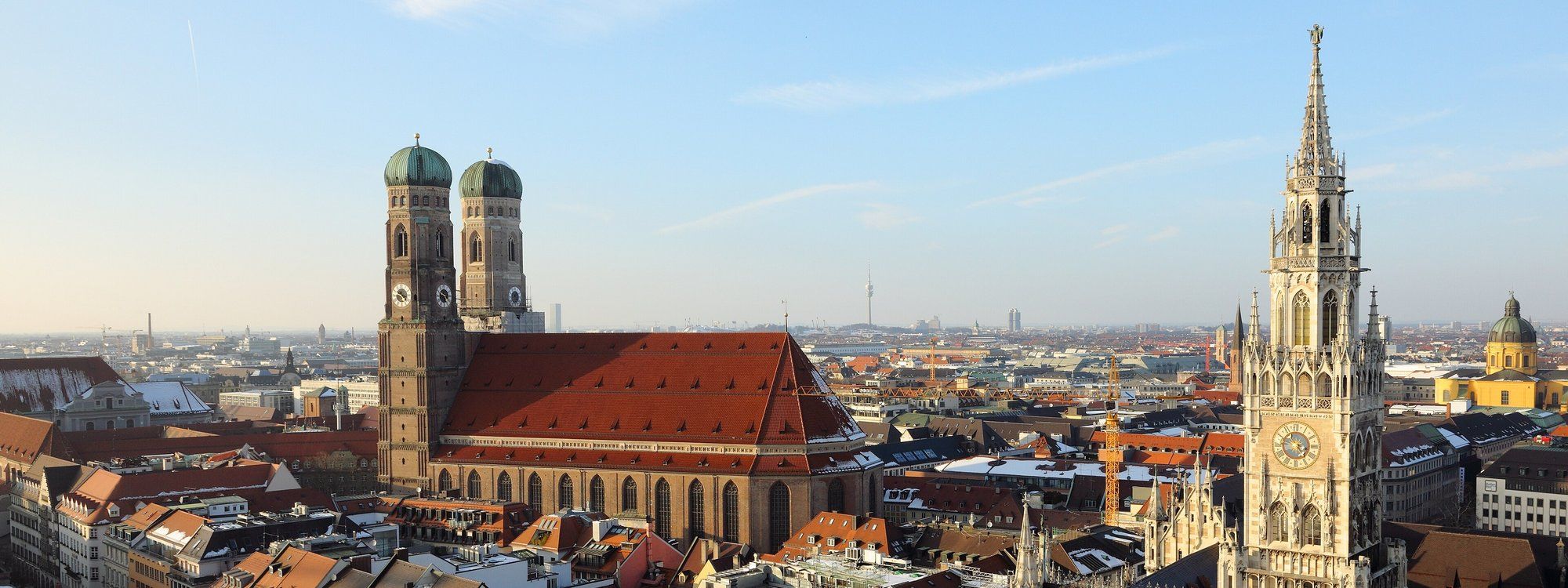 Rooftop view over Munich's old town, with the Frauenkirche's twin domes and the New Town Hall's tower rising above the red-tiled roofs