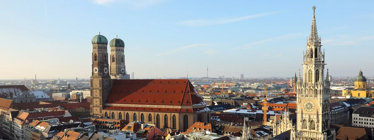 Rooftop view over Munich's old town, with the Frauenkirche's twin domes and the New Town Hall's tower rising above the red-tiled roofs