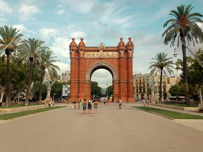 El arco de ladrillo rojo del Arc de Triomf, flanqueado por palmeras a lo largo del Passeig de Lluís Companys