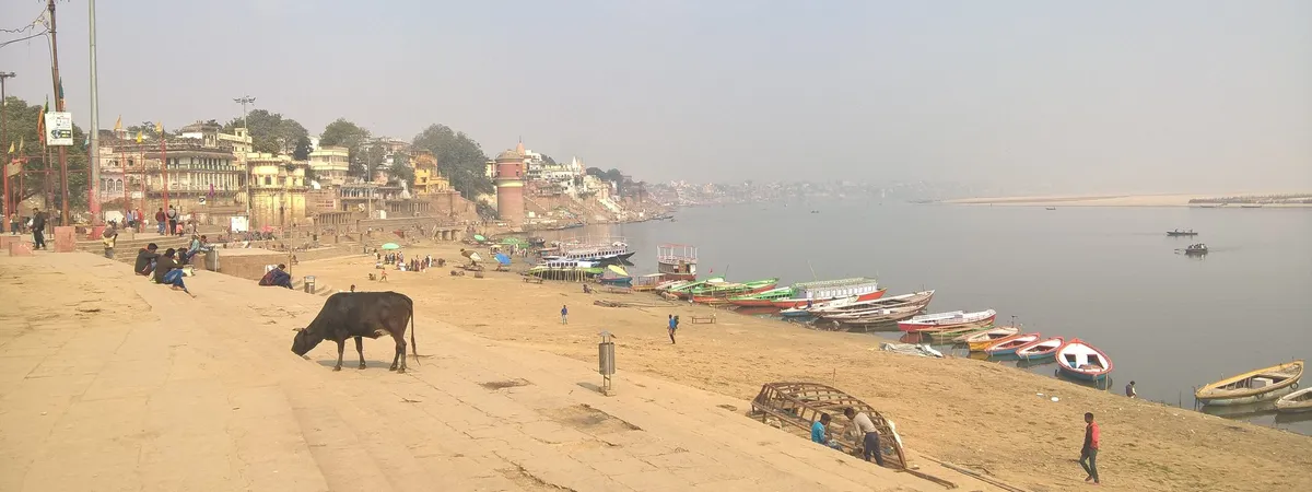 Assi Ghat's wide riverside steps and boats along the Ganges, with the old city skyline in the distance