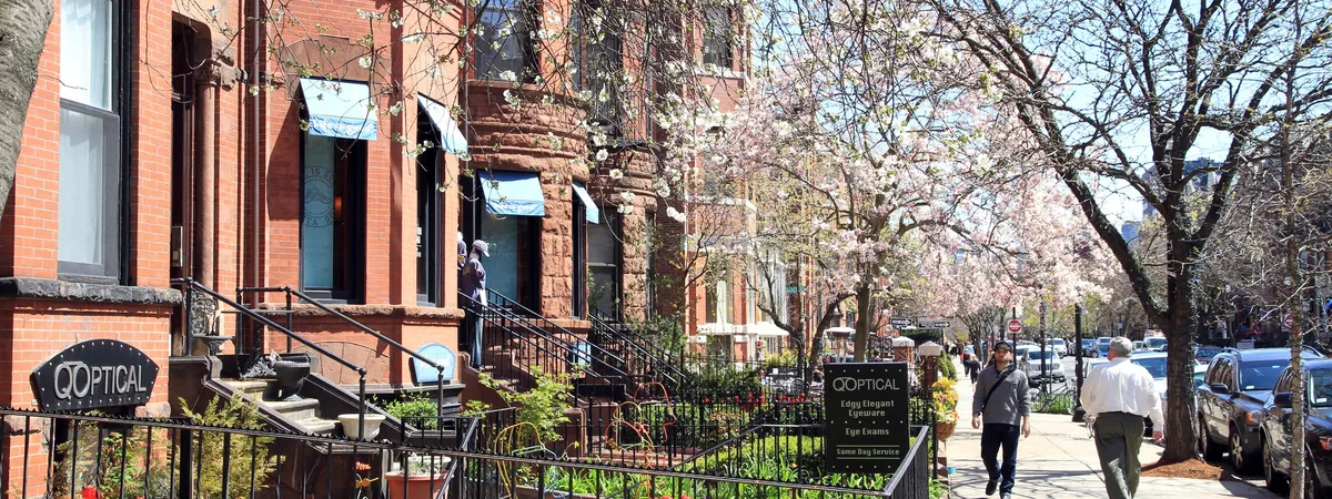 Bow-front brick brownstones and blossoming trees along Newbury Street in Back Bay, with people walking the sidewalk