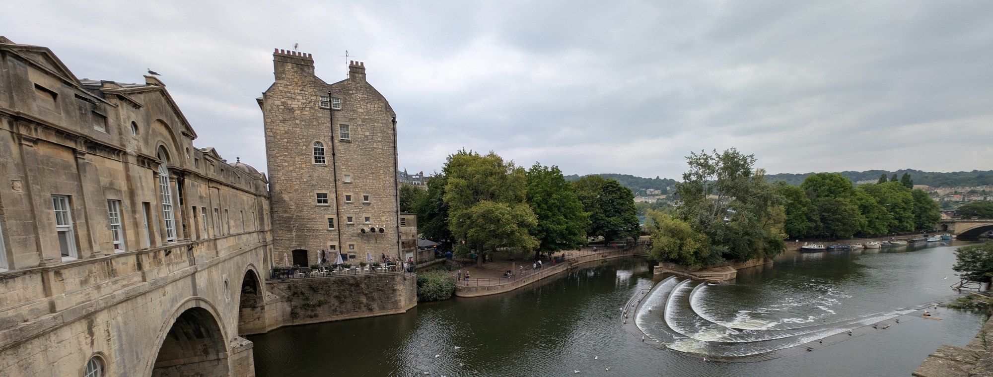 Pulteney Bridge and the horseshoe-shaped weir on the River Avon in Bath, seen from the bridge on an overcast day