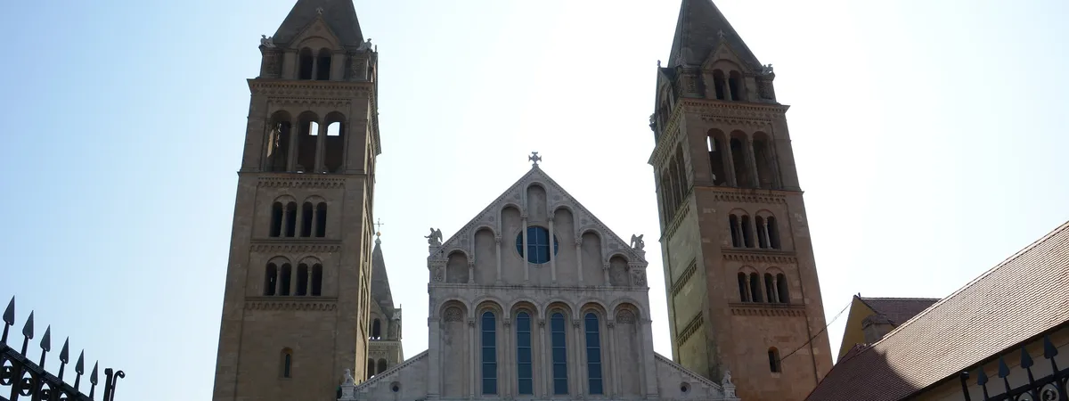 The twin Romanesque bell towers and gabled facade of Pécs Cathedral rising above the historic center