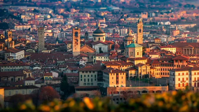 The towers and domes of Bergamo's Citta Alta at golden hour, with the lower town spread out behind
