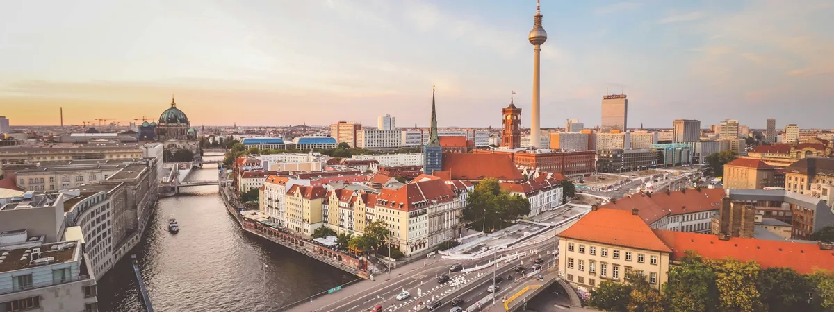 Golden-hour view over central Berlin from above, with the dome of Berlin Cathedral and the River Spree on the left and the red-brick Rotes Rathaus and Fernsehturm rising over Mitte