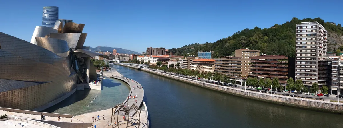 The titanium curves of the Guggenheim Museum Bilbao alongside the Nervión River, with the city and green hills behind