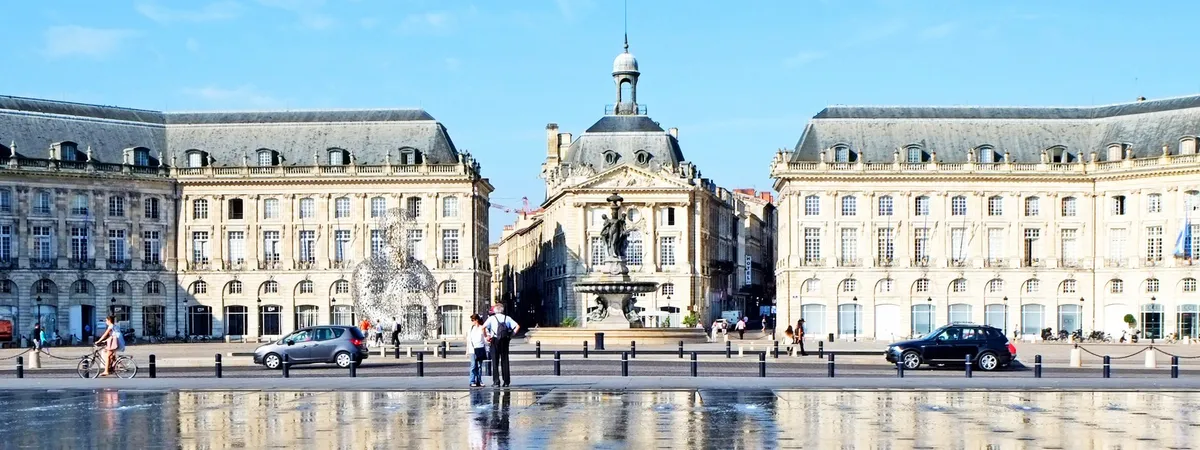 Place de la Bourse in Bordeaux reflected in the Miroir d'eau, with the Three Graces fountain and the city's 18th-century stone facades behind