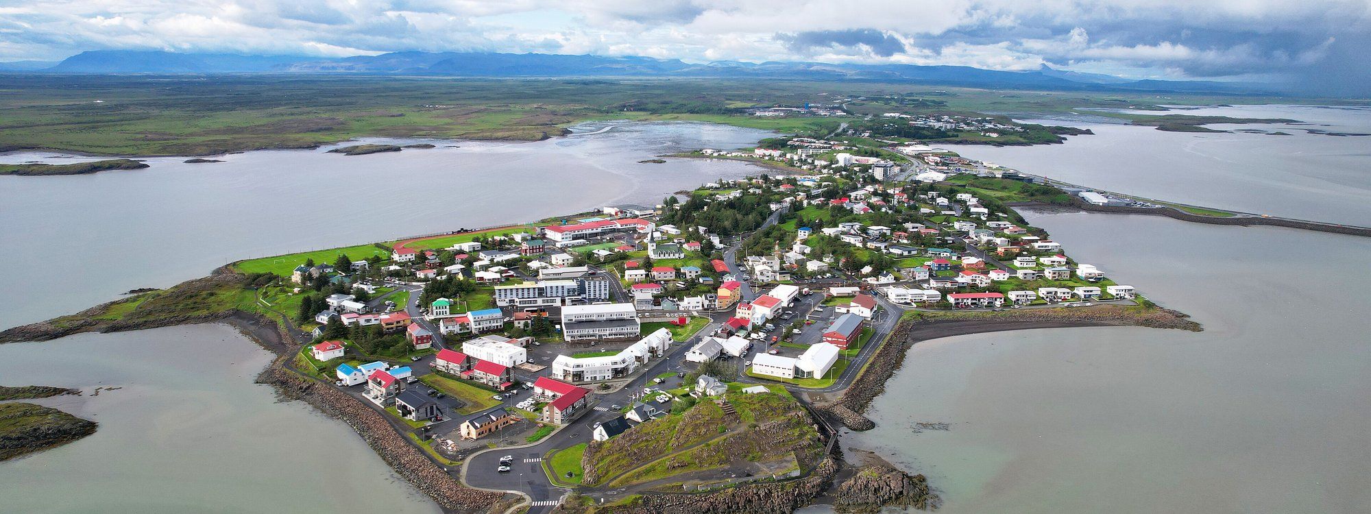 Aerial view of Borgarnes on its narrow peninsula in Borgarfjörður, with the old town clustered at the tip and mountains behind
