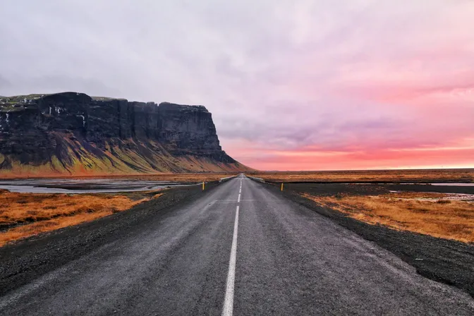 The Ring Road stretching toward dramatic cliffs under a pink sunset sky in west Iceland