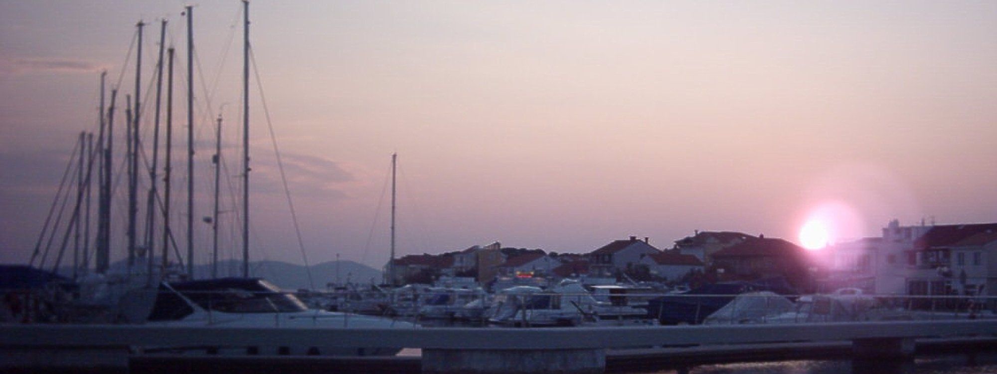 Sailboats and motor yachts moored at Marina Borik at dusk, with Zadar's coastline in the background