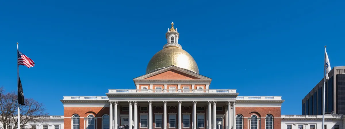 The Massachusetts State House's golden dome and columned façade on Beacon Hill, seen straight-on against a clear sky