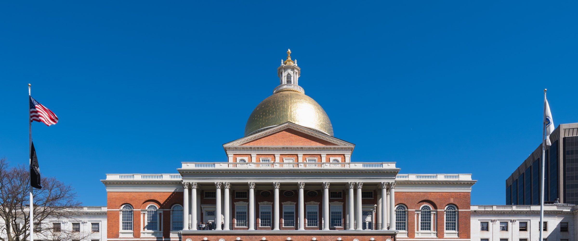 The Massachusetts State House's golden dome and columned façade on Beacon Hill, seen straight-on against a clear sky