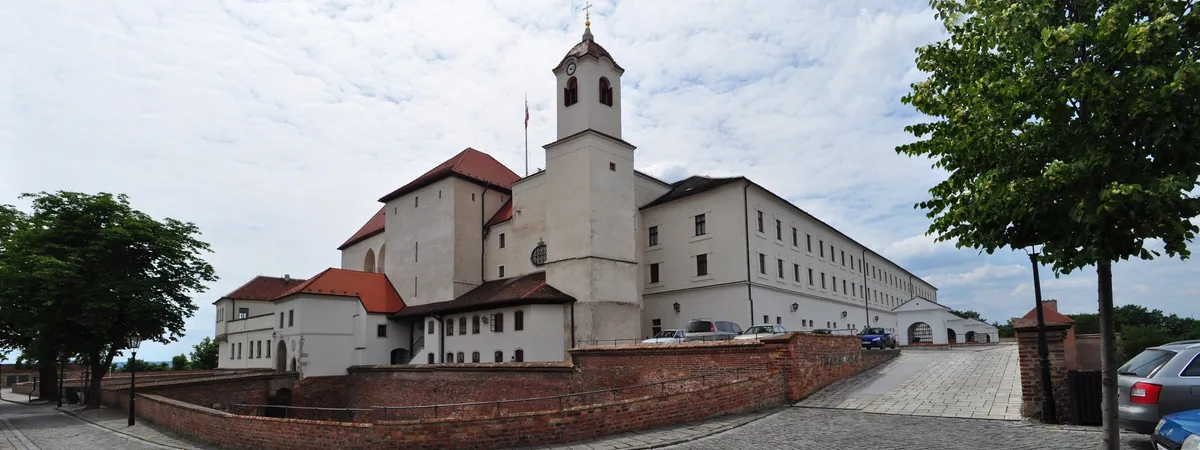 Špilberk Castle's white walls, red-tiled roofs, and clock tower rising above its brick fortifications on the hill above Brno