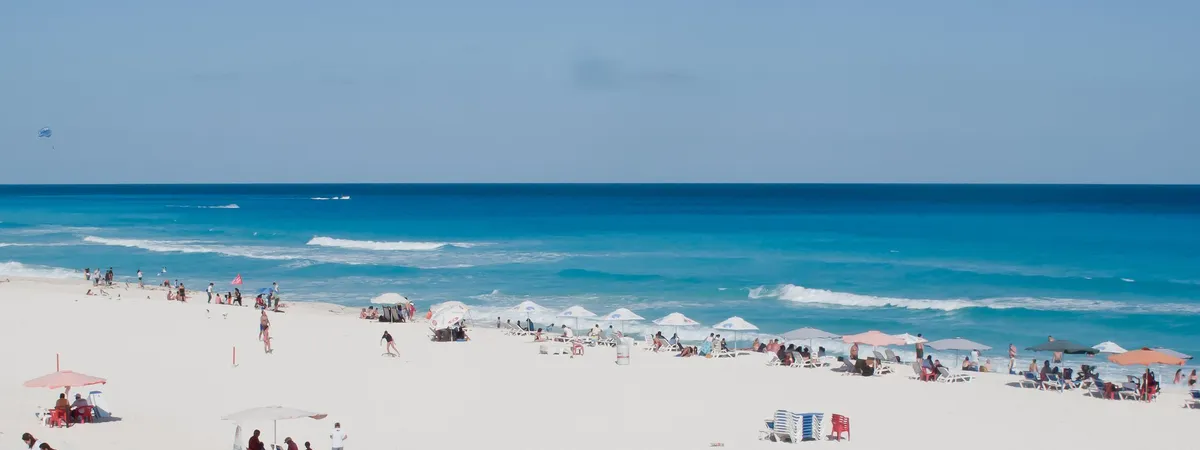 Sunbathers and beach umbrellas along the white sand and turquoise water of Playa Delfines, Cancún
