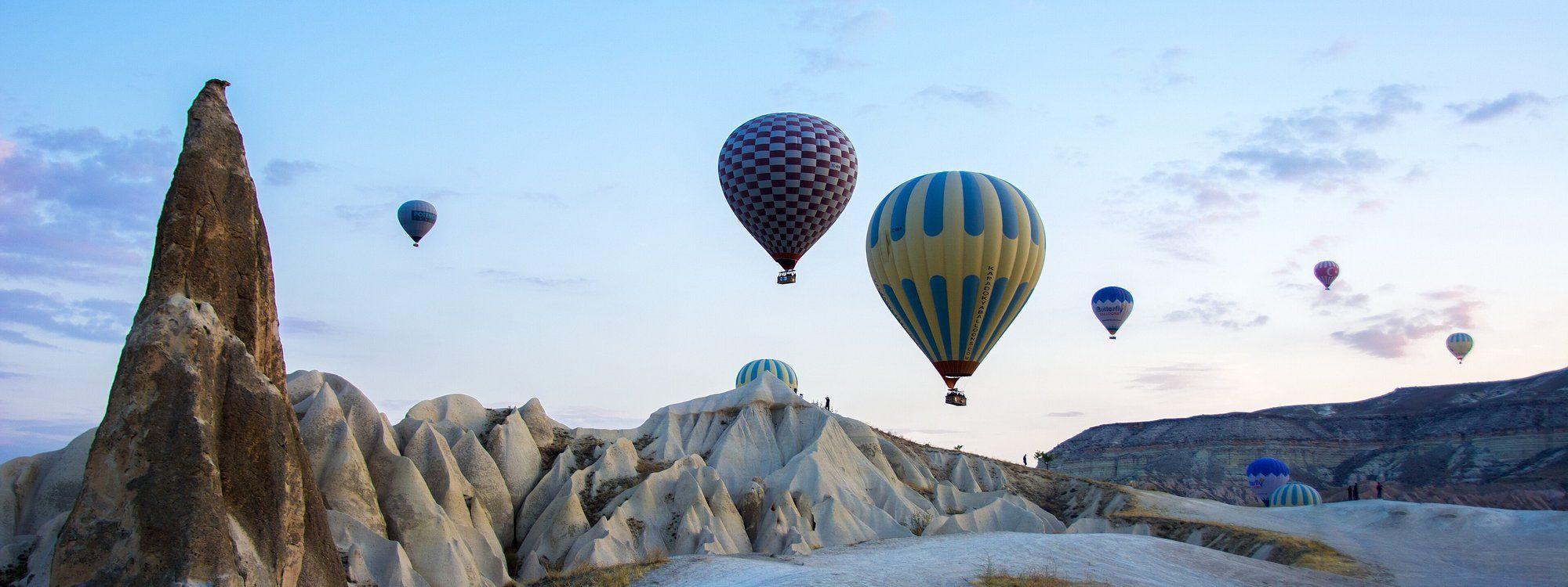 Dozens of hot air balloons rising at dawn over Cappadocia's cone-shaped fairy chimney rock formations