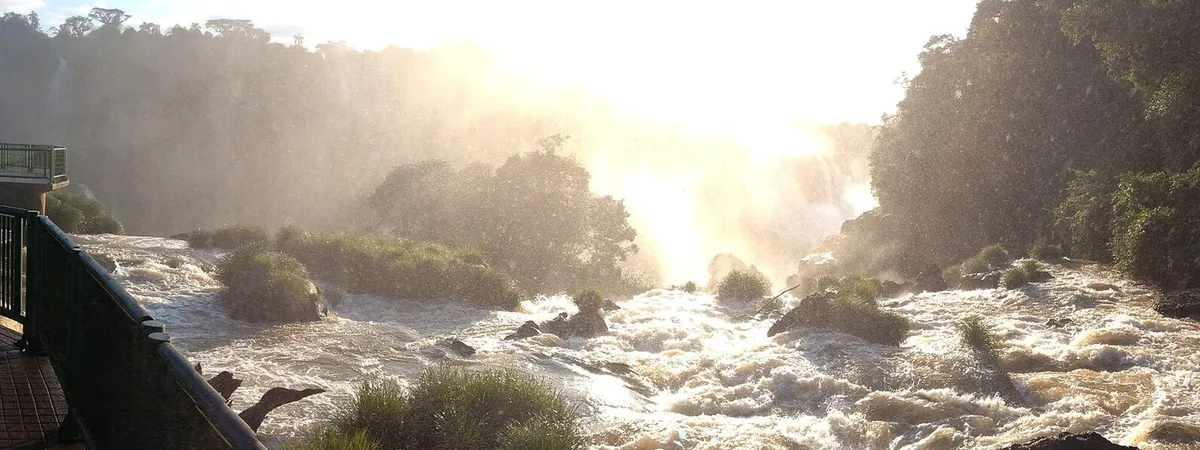 Neblina elevándose sobre la Garganta del Diablo en las Cataratas del Iguazú, vista desde la pasarela del lado brasileño, con el sol filtrándose entre el rocío