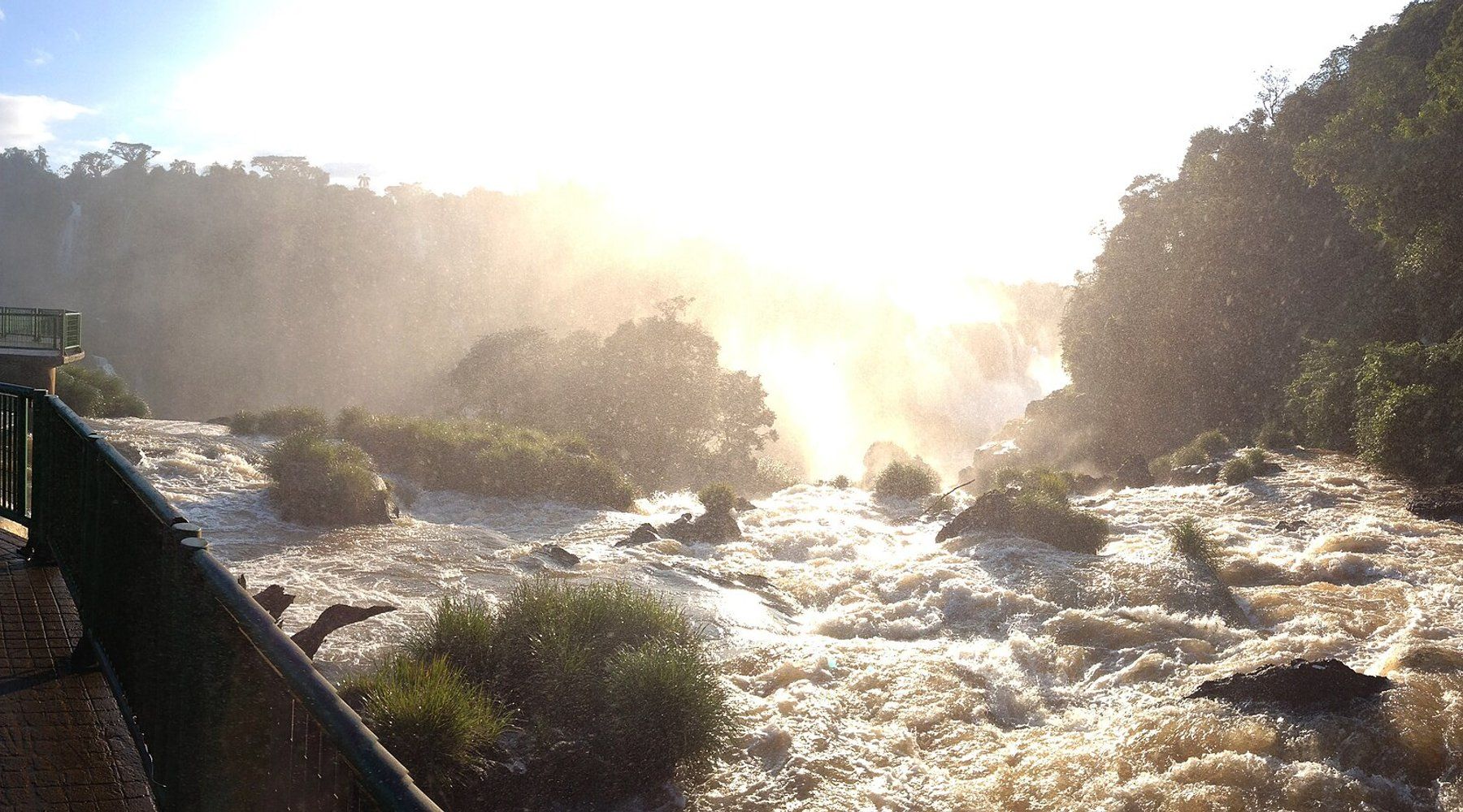 Neblina elevándose sobre la Garganta del Diablo en las Cataratas del Iguazú, vista desde la pasarela del lado brasileño, con el sol filtrándose entre el rocío