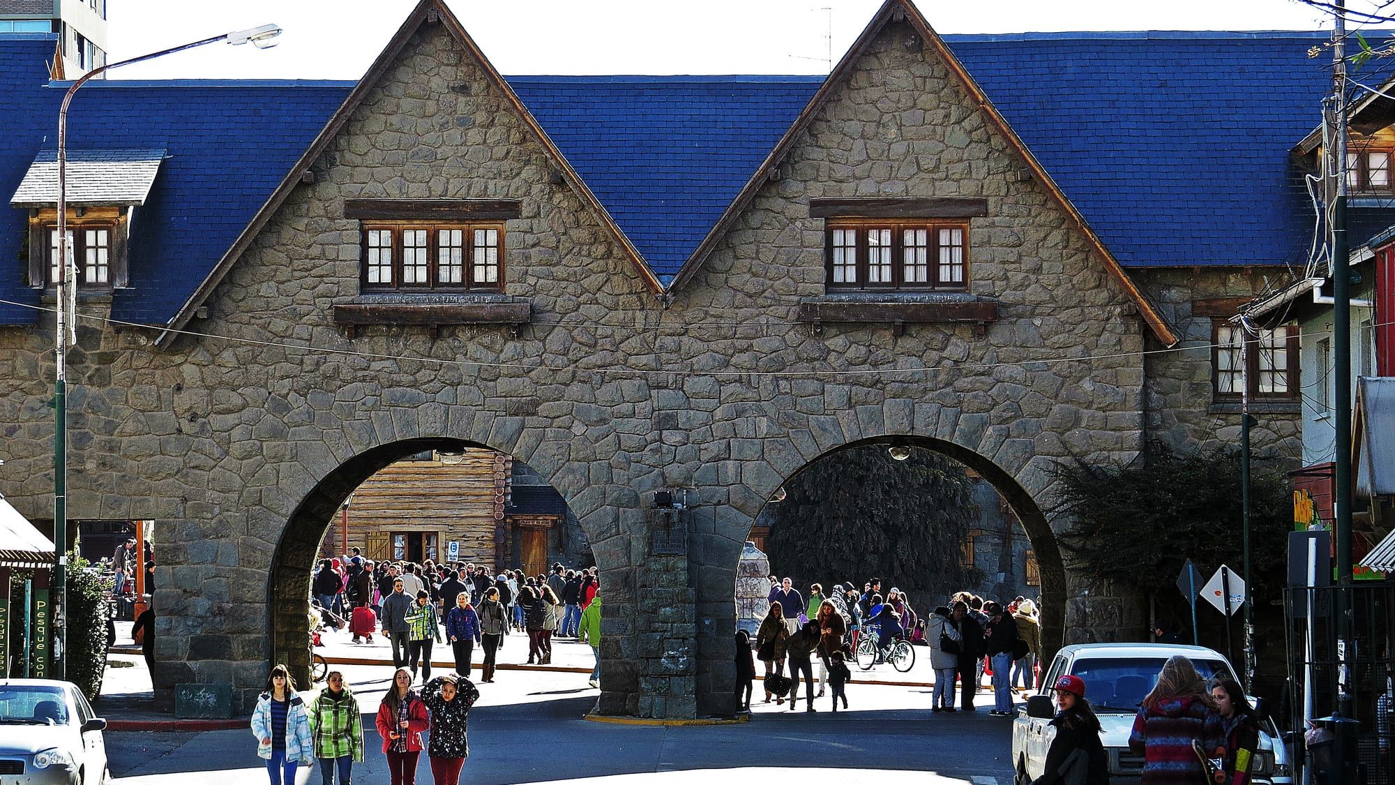 The stone archways of Bariloche's Centro Cívico complex, with crowds of visitors passing through on a sunny day