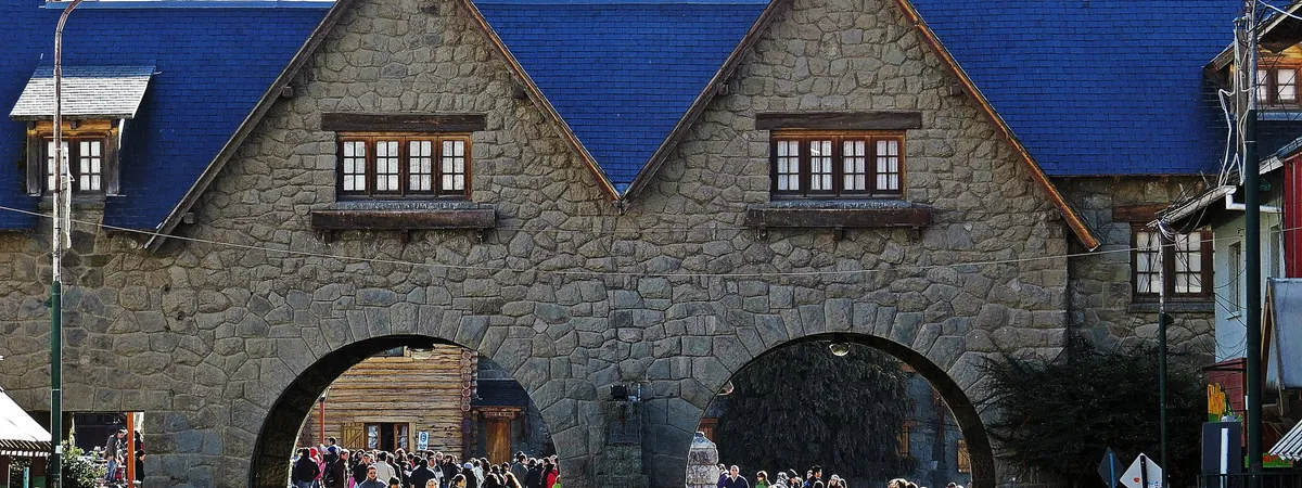 The stone archways of Bariloche's Centro Cívico complex, with crowds of visitors passing through on a sunny day