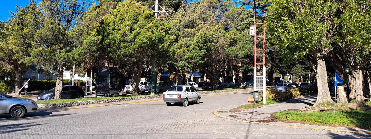 Un tramo arbolado de la Avenida del Libertador en el centro de El Calafate, con autos estacionados a lo largo de una calle empedrada