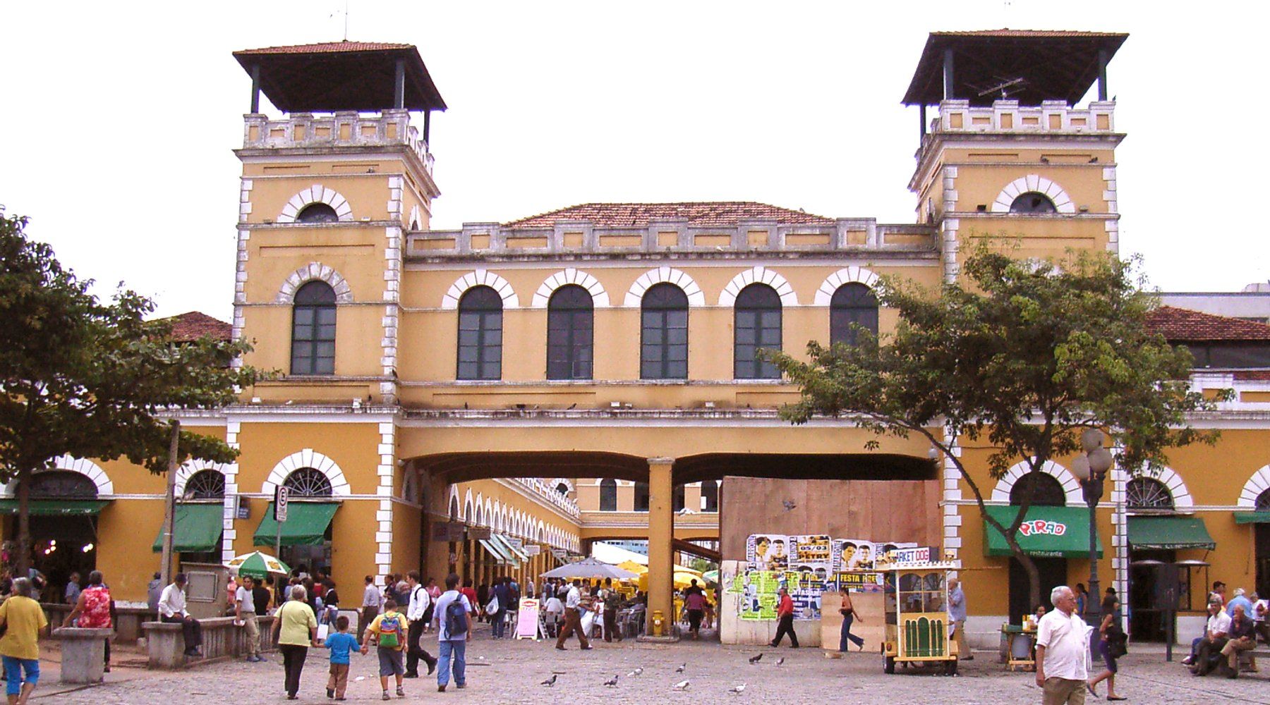 The yellow twin towers and covered walkway of the historic Mercado Público building in downtown Florianópolis, with visitors in the square outside
