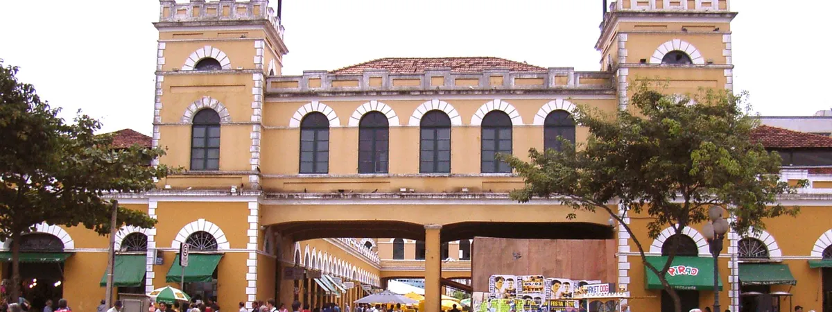 The yellow twin towers and covered walkway of the historic Mercado Público building in downtown Florianópolis, with visitors in the square outside