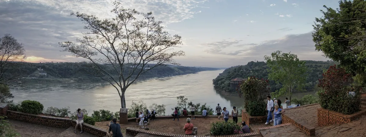 Visitors gather at sunset at the Hito Tres Fronteras viewpoint in Puerto Iguazú, overlooking the river where Argentina, Brazil, and Paraguay meet