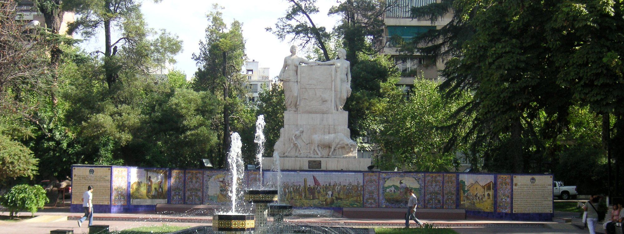 Plaza España's Spanish-tiled mosaic mural and fountain, with a stone monument and trees behind it, in downtown Mendoza