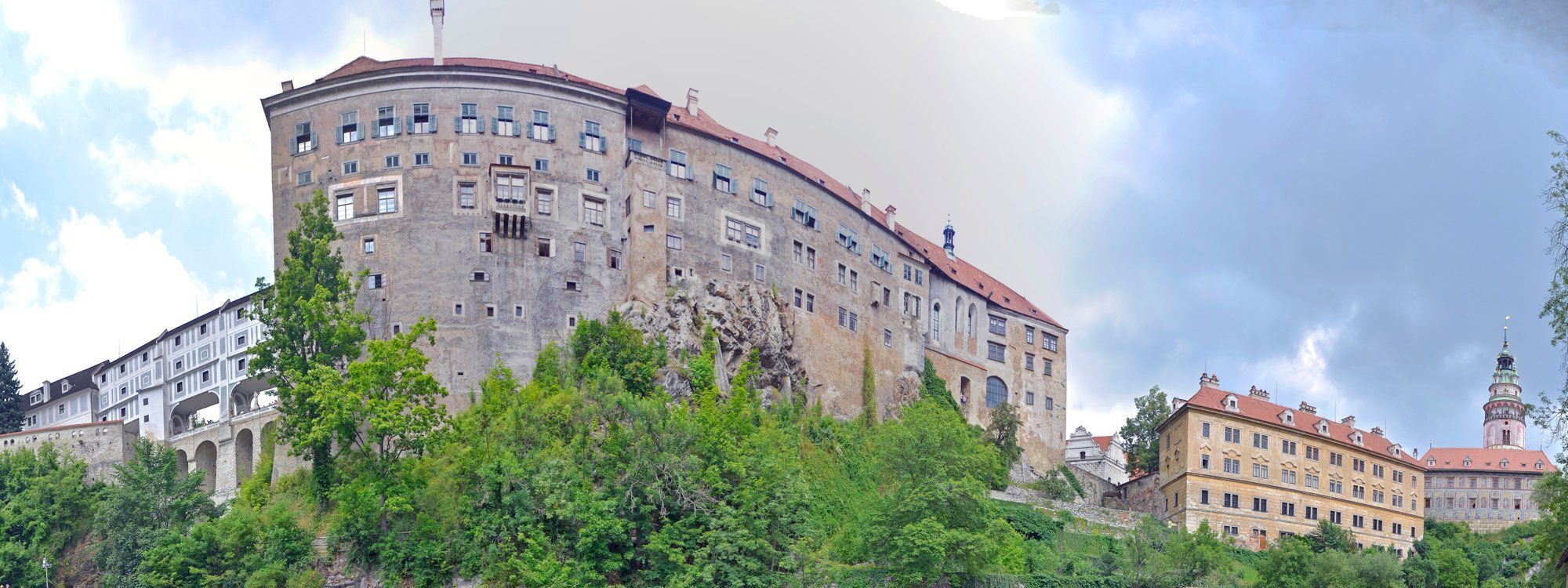 Elevated view of Český Krumlov Castle rising over the Vltava river, with the castle's colorful tower visible on the far side