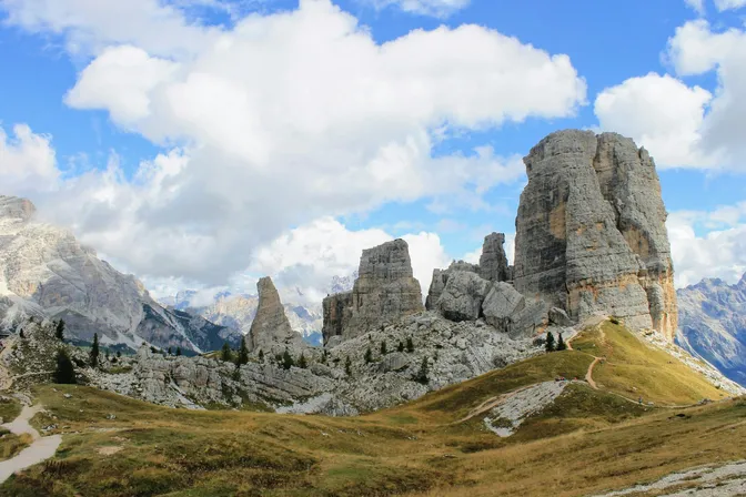 The Cinque Torri rock towers rising from grassy slopes above Cortina, with a walking path curving round them