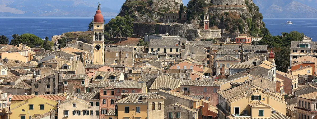 The Old Town of Corfu's terracotta rooftops and bell tower beneath the Old Fortress, with the Ionian Sea behind