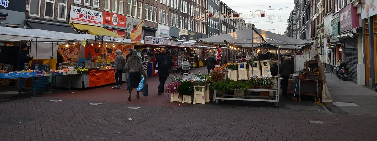 Market stalls selling flowers and produce along Albert Cuypstraat in De Pijp, with shoppers browsing
