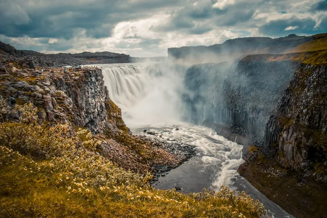 Dettifoss's wide, powerful cascade thundering into its canyon, visitors watching from the rim