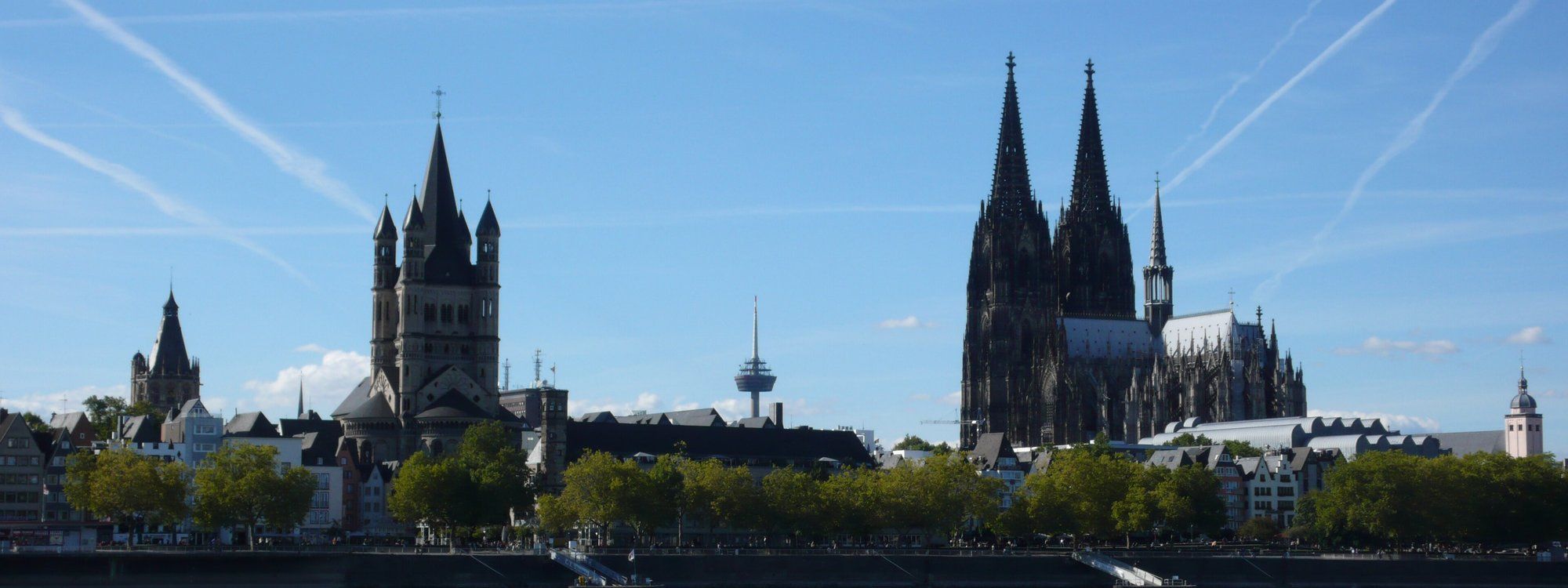 View across the Rhine from the Rheinboulevard in Deutz toward Cologne's old town, with Groß St. Martin and the cathedral's spires on the skyline