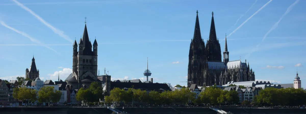View across the Rhine from the Rheinboulevard in Deutz toward Cologne's old town, with Groß St. Martin and the cathedral's spires on the skyline