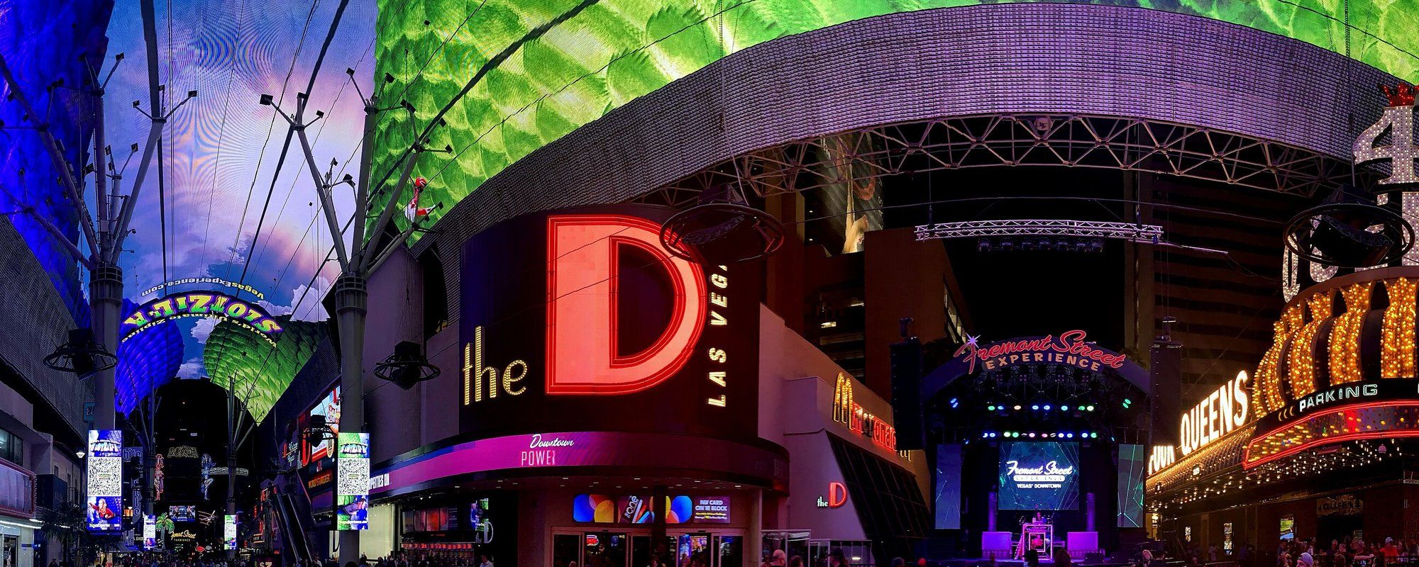 The Fremont Street Experience canopy lit up at night in downtown Las Vegas, with the D Las Vegas and Fremont Street Experience signs visible below