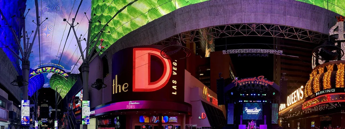 The Fremont Street Experience canopy lit up at night in downtown Las Vegas, with the D Las Vegas and Fremont Street Experience signs visible below