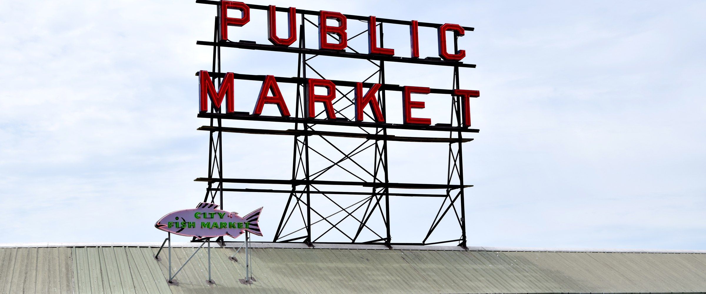 השלט האדום הניאון 'Public Market' ושלט דג City Fish Market מעל דוכני פייק פלייס מרקט בדאונטאון סיאטל
