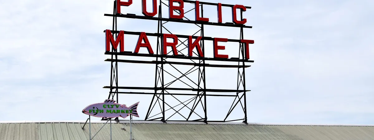 השלט האדום הניאון 'Public Market' ושלט דג City Fish Market מעל דוכני פייק פלייס מרקט בדאונטאון סיאטל
