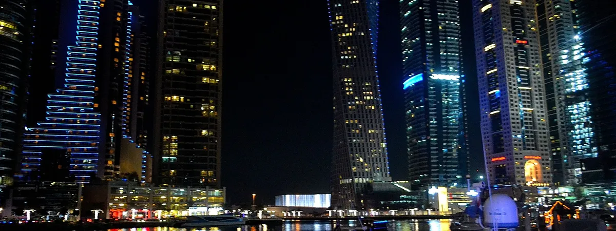 Dubai Marina's skyline at night, including the twisting Cayan Tower, reflected in the marina waters