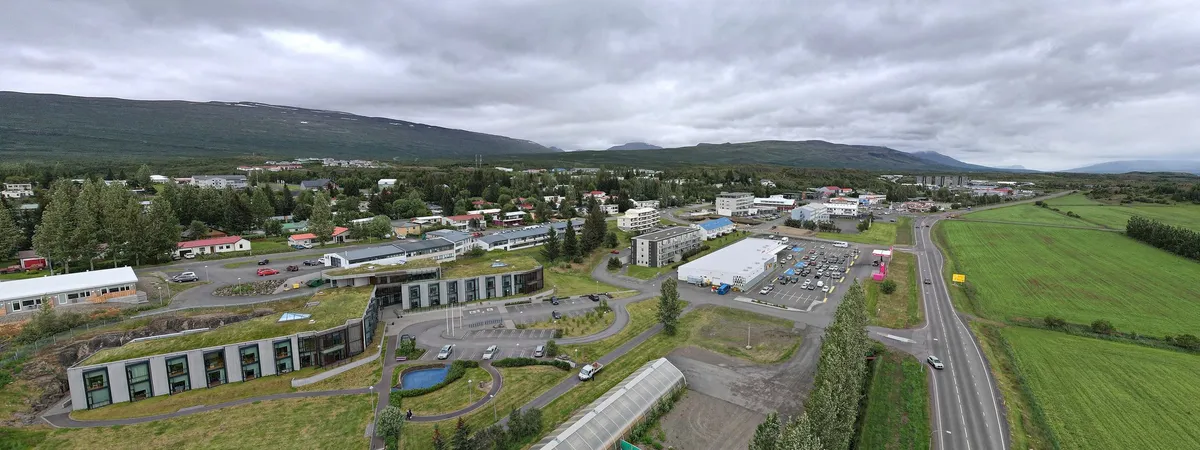 Aerial view of Egilsstaðir's town center, with low modern buildings, a supermarket and car parks, set against green hills and mountains