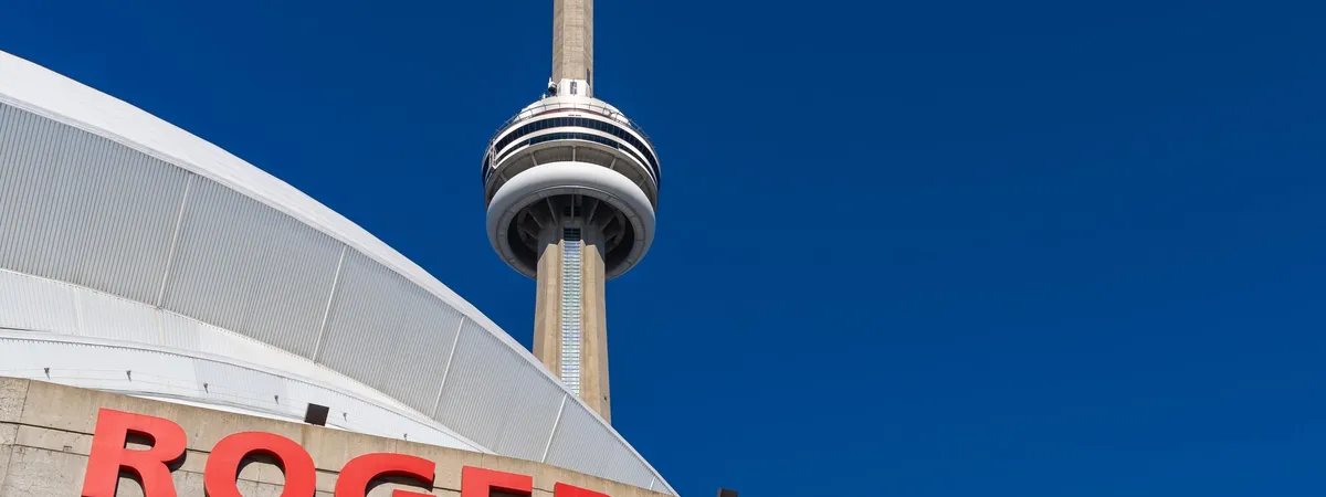 The CN Tower rising behind the curved roof and red Rogers Centre sign in downtown Toronto