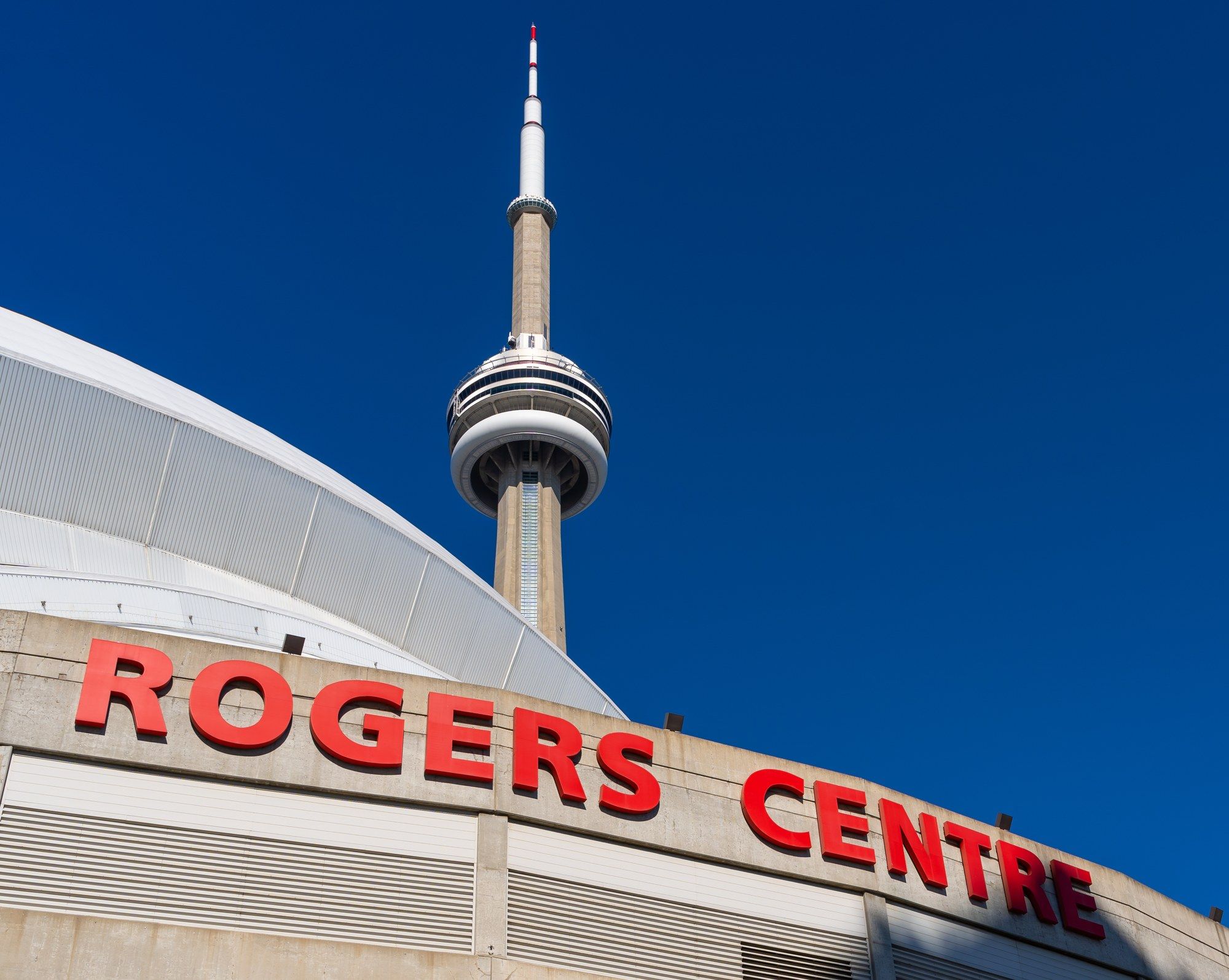 The CN Tower rising behind the curved roof and red Rogers Centre sign in downtown Toronto