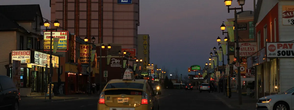 Clifton Hill's neon-lit entertainment strip at dusk, lined with hotels, restaurants, and souvenir shops leading downhill toward the falls