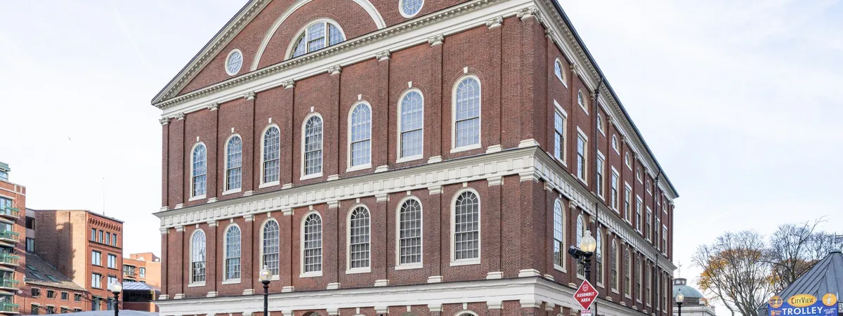 Faneuil Hall's brick Georgian façade with trolley-tour signs and outdoor benches in the plaza below