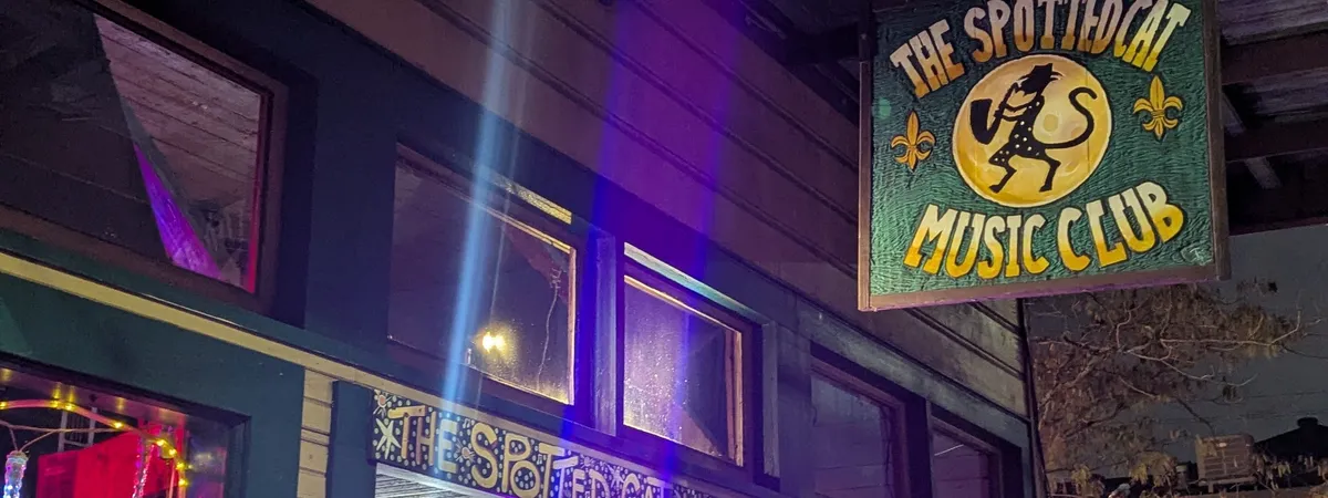The hand-painted sign for The Spotted Cat Music Club lit up at night on Frenchmen Street in Faubourg Marigny